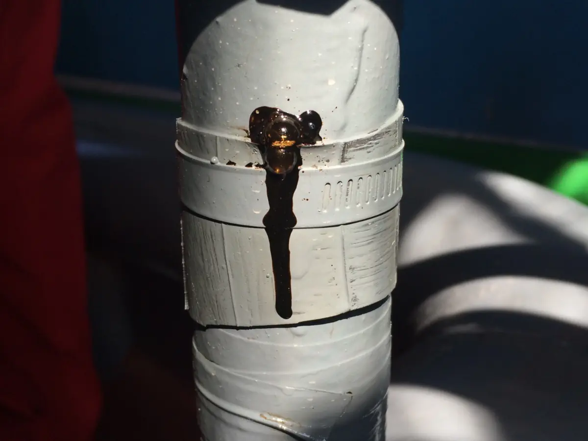 Dark liquid leaking from a prior clamp and plastic-pad arrangement on a vertical steel pipe